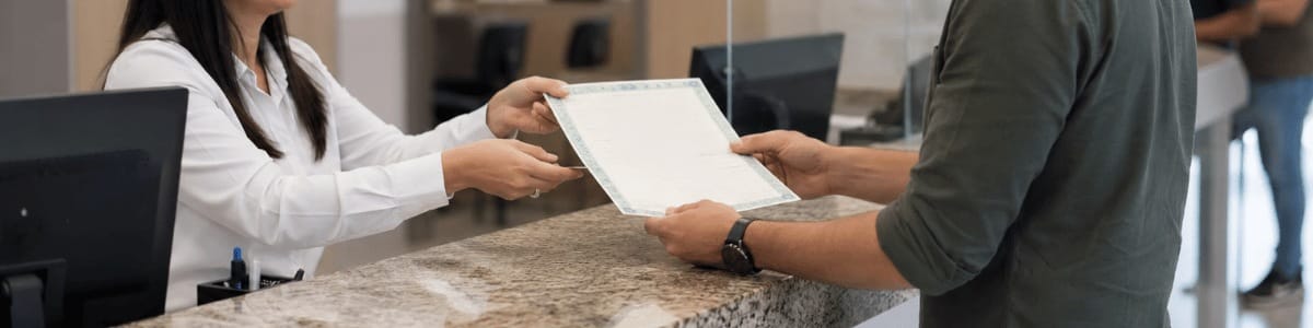 Pessoa recebendo uma certidão de uma atendente em um cartório, em um ambiente profissional e bem iluminado.