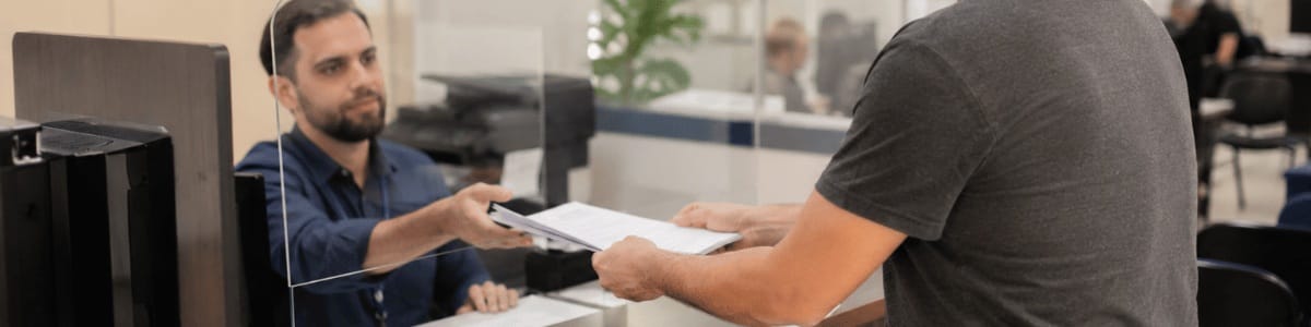 Pessoa entregando documentos a um atendente em uma prefeitura, em um ambiente público organizado e iluminado, transmitindo seriedade, atendimento institucional e orientação ao cidadão.