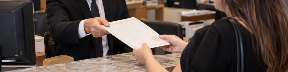 Funcionário de cartório entregando uma certidão a uma cliente em um ambiente de atendimento profissional e acolhedor