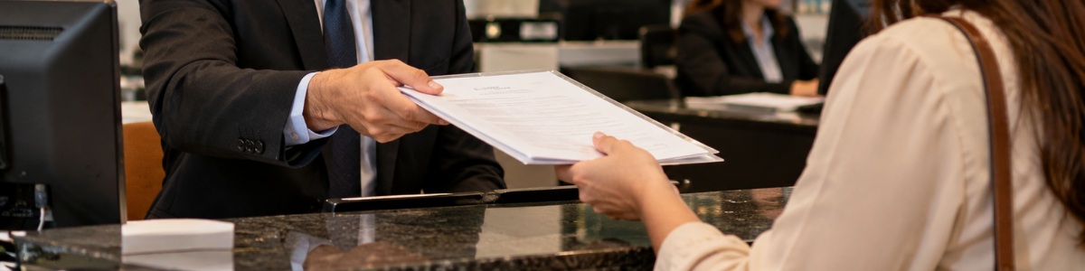 Funcionário do cartório de imóveis entrega um documento ao cliente em um atendimento profissional, em ambiente interno organizado e acolhedor.